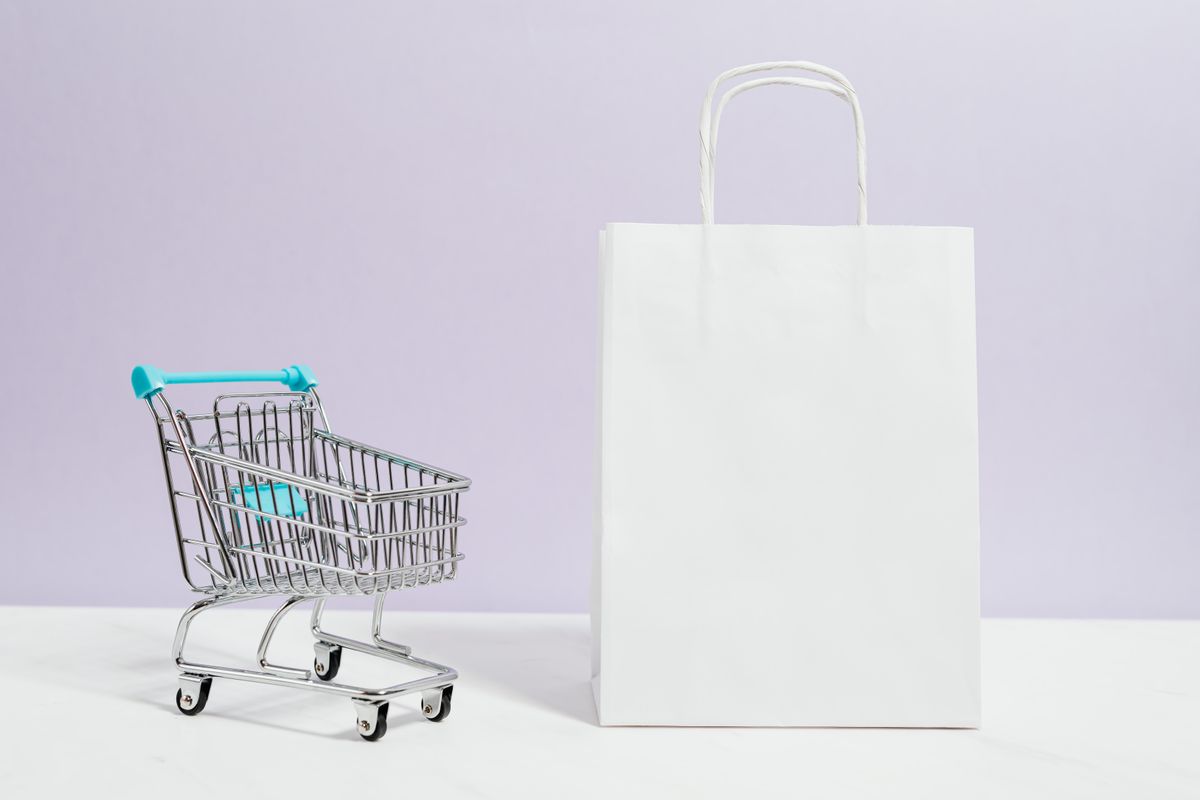 A miniature shopping trolley beside a paper shopping bag